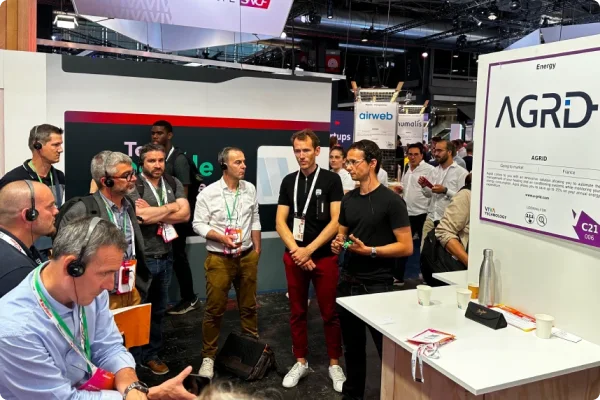 Jean-Pierre, président R&D d’AGRID, présente la technologie AGRID sur le stand d’un salon, devant un groupe de visiteurs